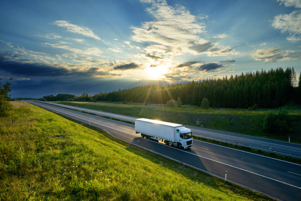 A truck driving along a road with a vibrant sunset in the background, casting warm colors across the sky.
